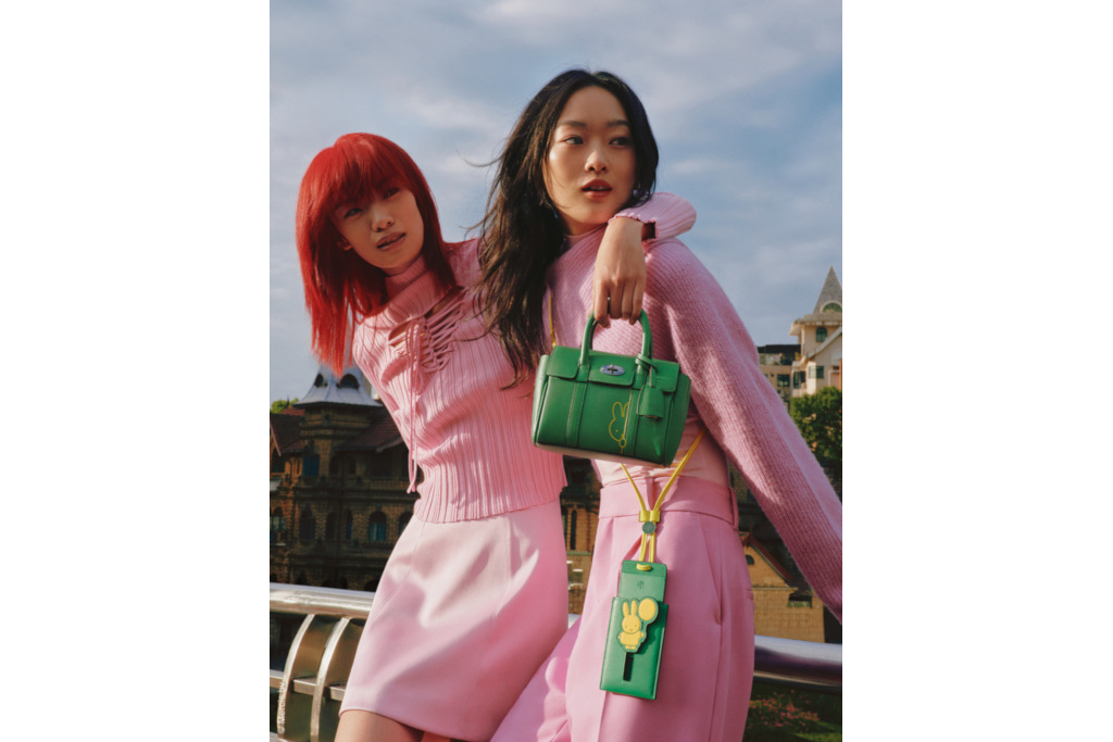 Two models in pink holding bags as they lean on railing