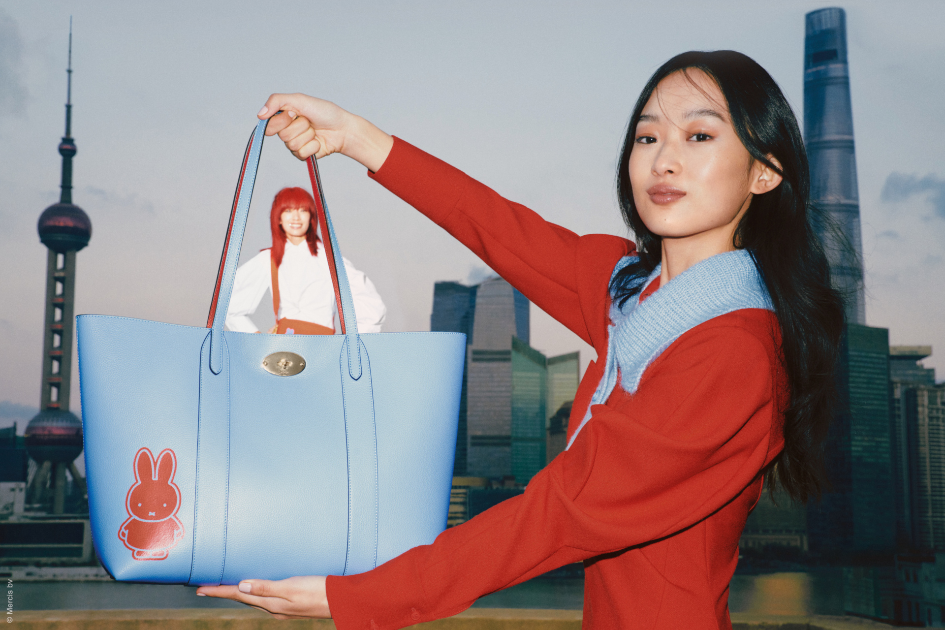 Woman holding up blue bag to show another woman in the background
