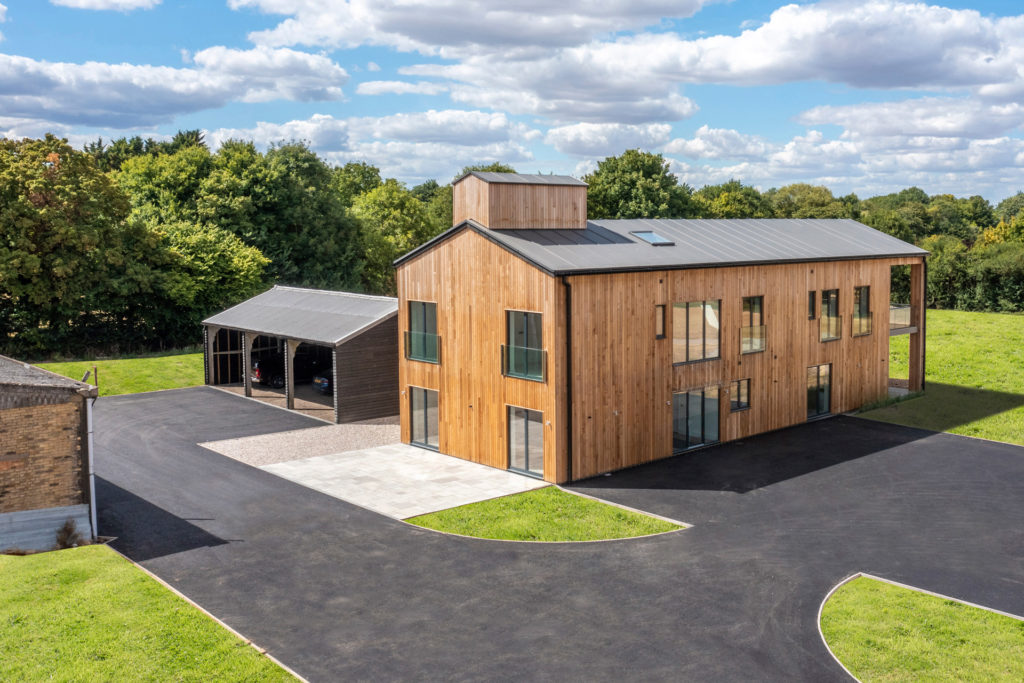 Prairie Barn, Hitchin. Wood-panelled exterior with a large black barn and further outbuilding, all surrounded by fields.