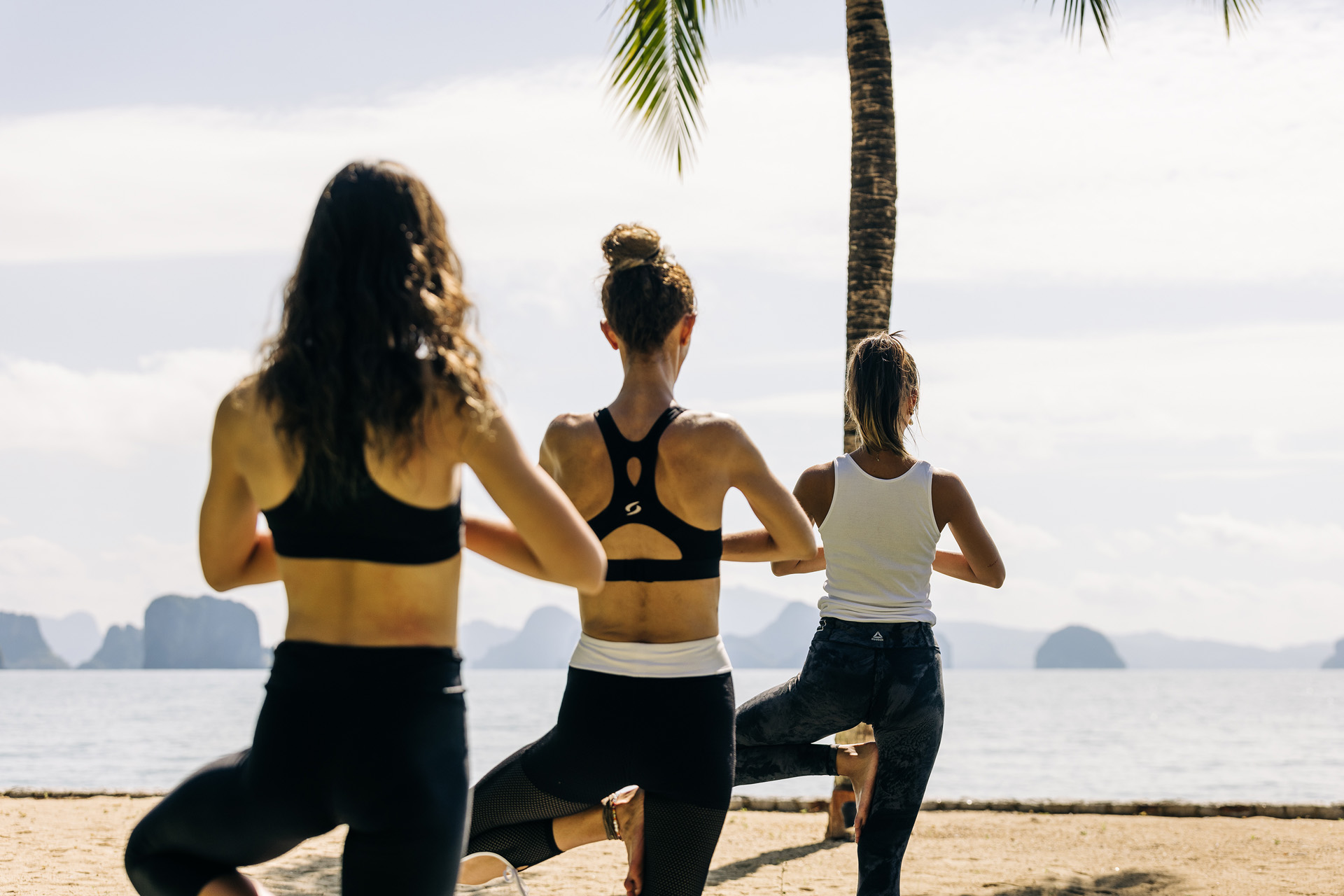 Three people in tree pose on the beach
