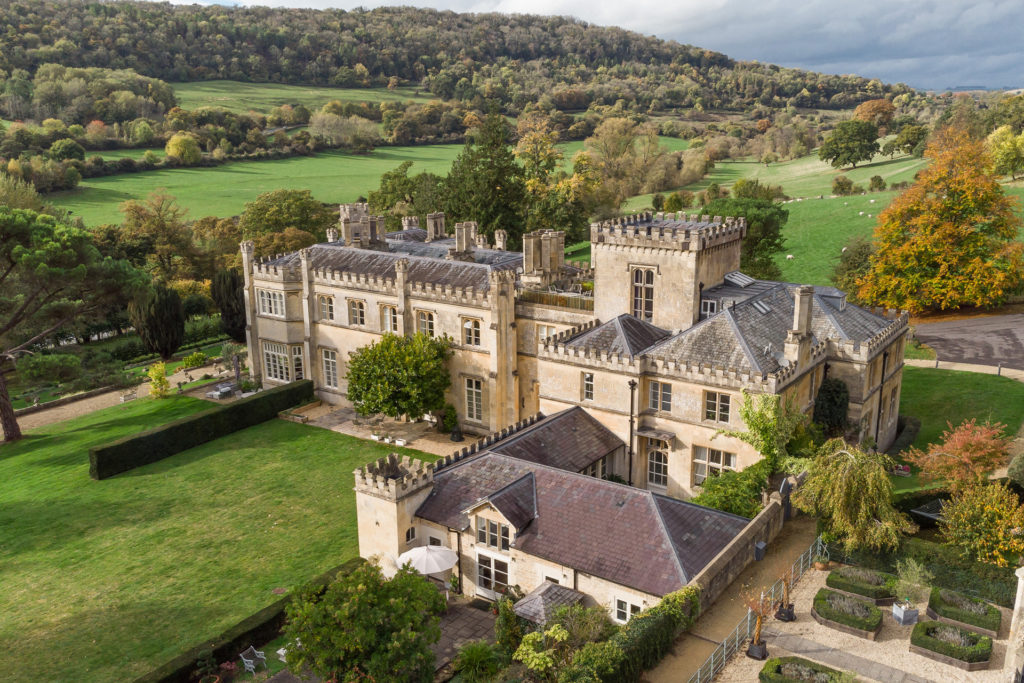 Exterior of Warleigh Manor, Bath, which features brick turrets and valleys beyond.