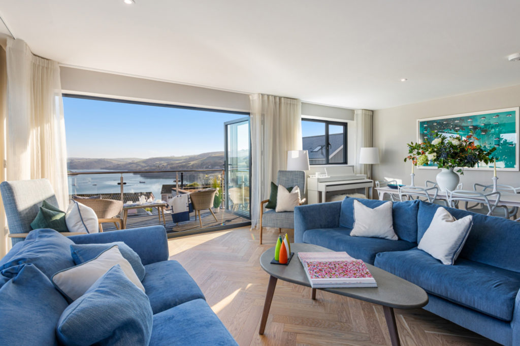 Living room with blue sofas and a large window with a view of sandy beaches and an estuary.