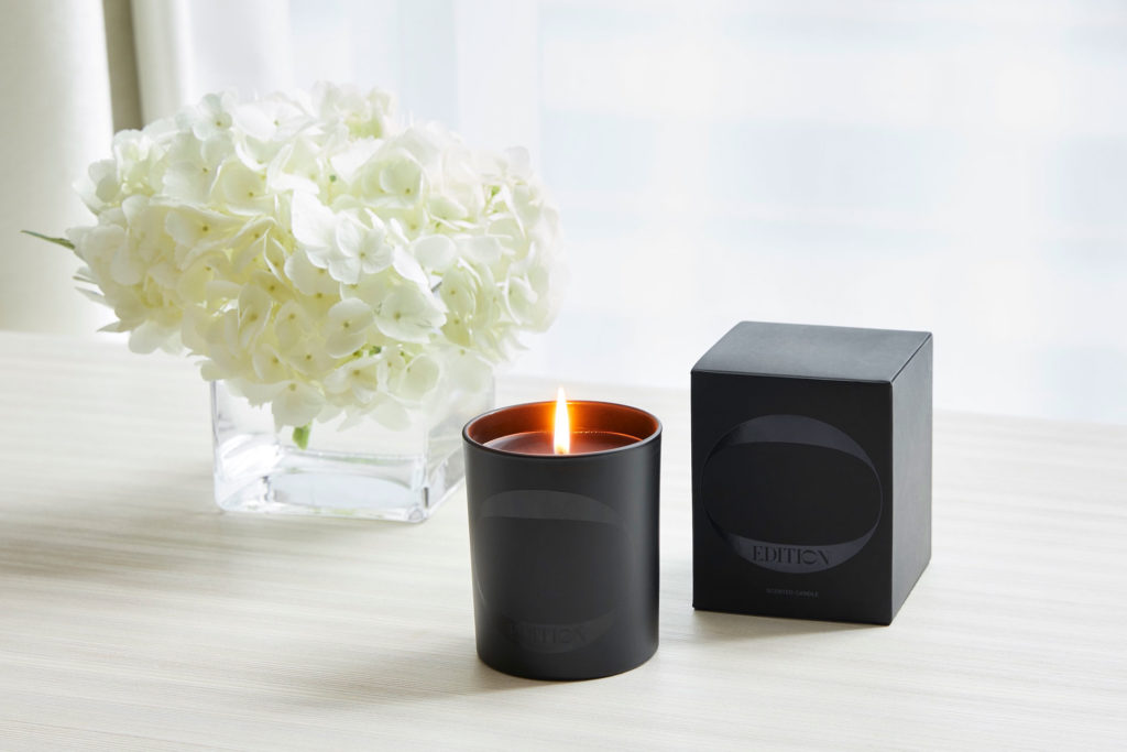 Black EDITION candle next to a vase of white flowers