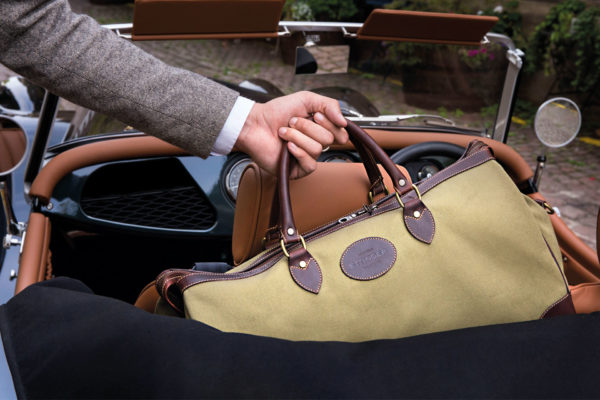 A person grabbing an Ettinger-branded hold-all from an old school car | british men's bag brands
