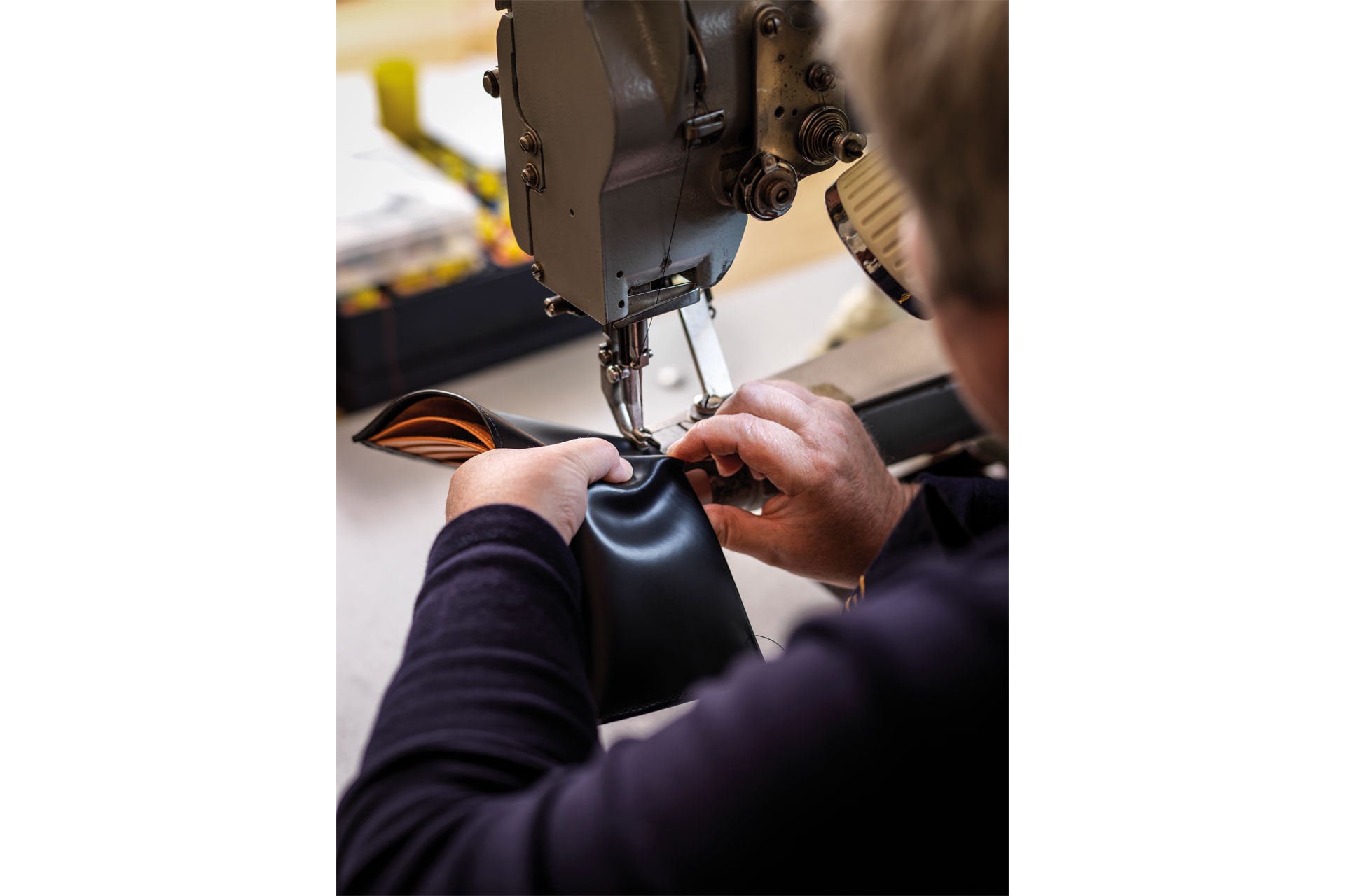 A person stitching a leather item together with professional machinery