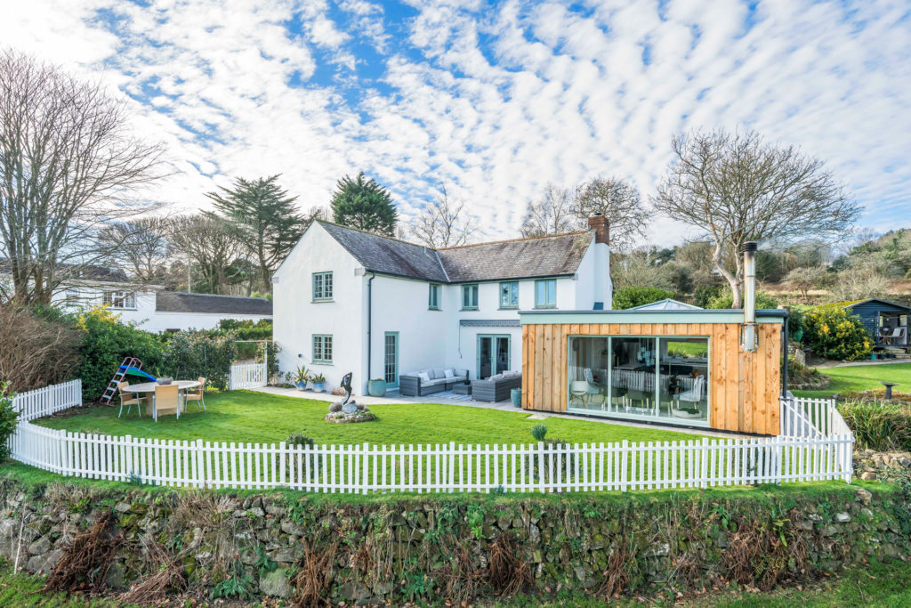 Exterior of Holly Tree Farm, Fernsplatt, Cornwall, with white painted brick and a kitchen extension with wood panelling.