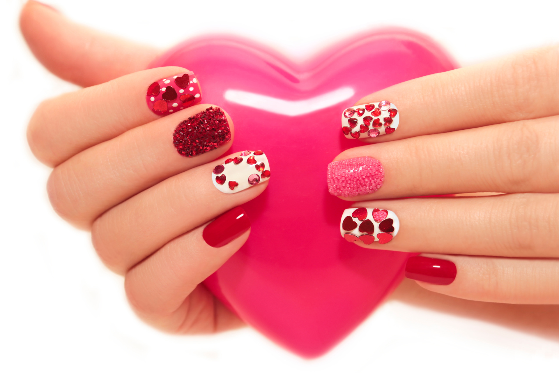 Manicure with rhinestones in the shape of hearts and pink balls on white and red nail Polish on a white background.
