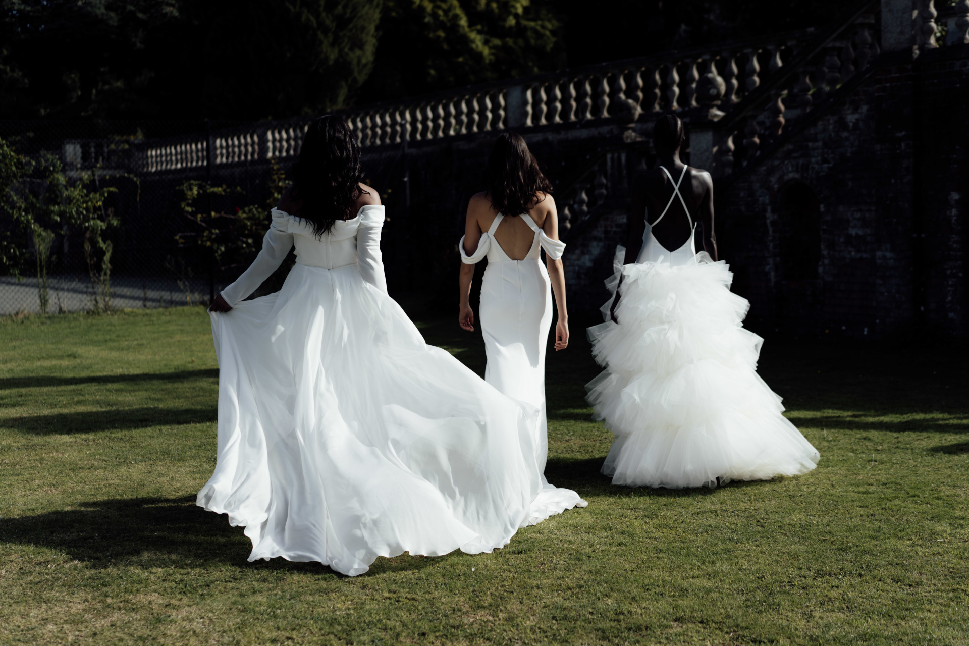 Three women in wedding dresses walking away on grass