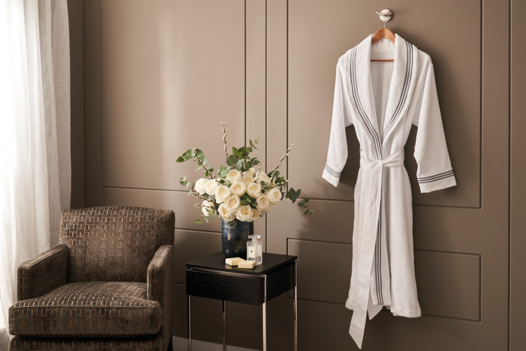 Bathrobe hung up on wall by brown armchair and side table with flowers