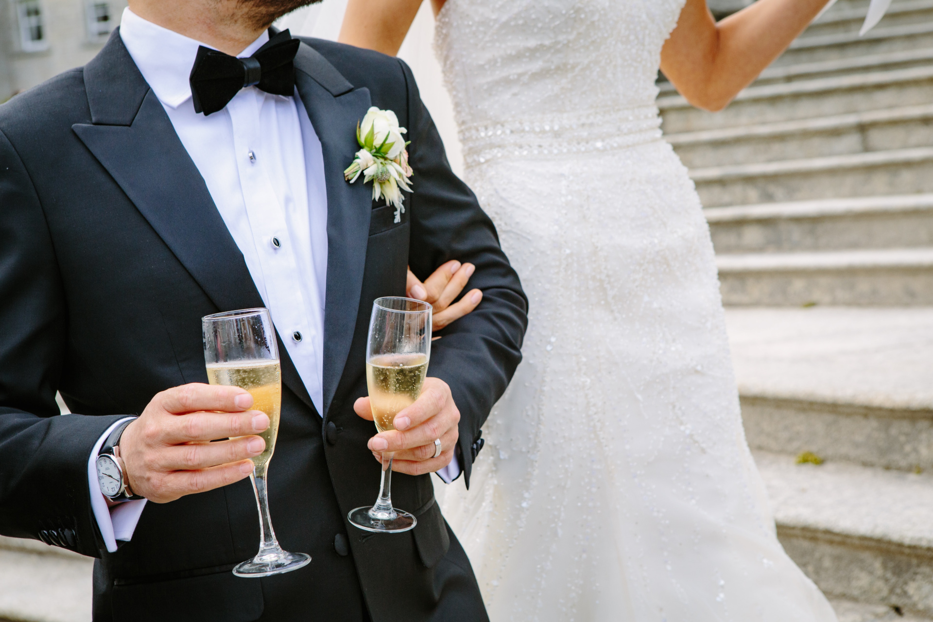 Close up of bride and groom walking down steps holding glasses of champagne