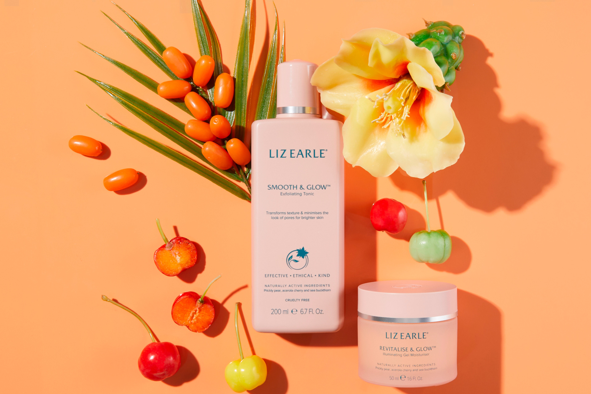 Pink skincare bottle on orange background with fruit and flowers