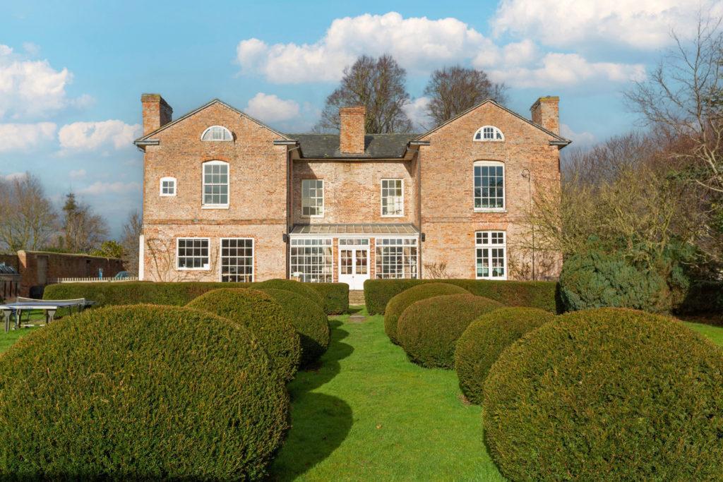 Exterior of Llandrinio Hall, with landscaped gardens and hedges in the foreground.
