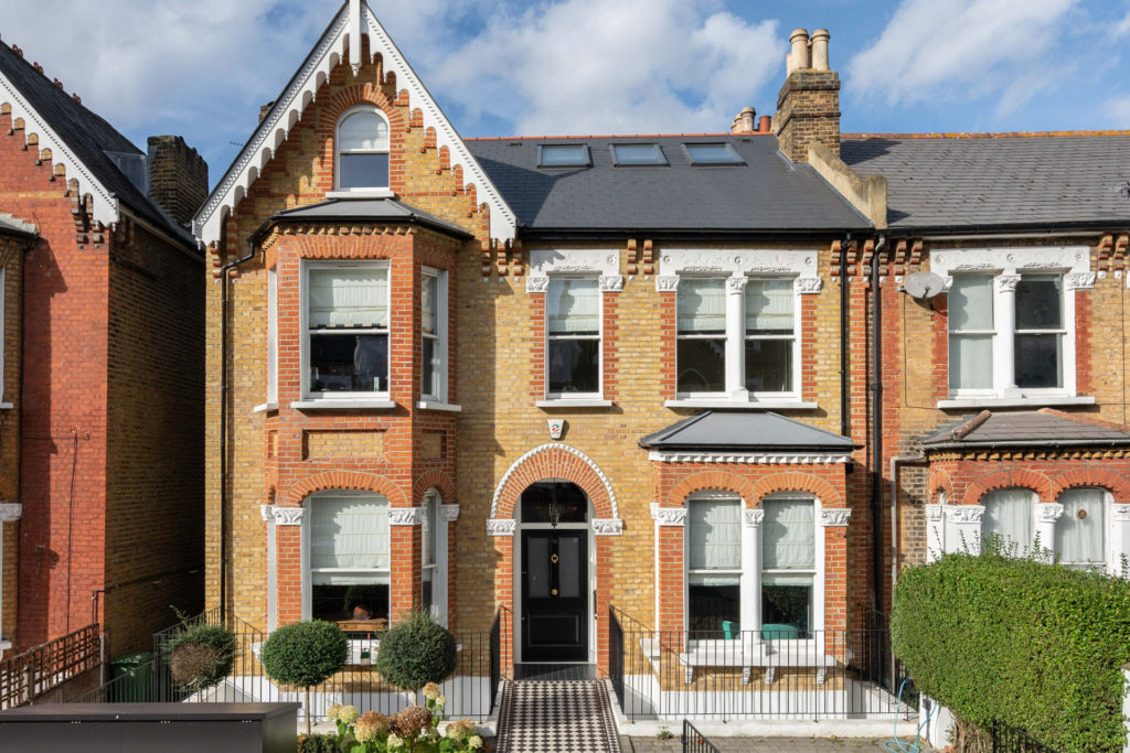 Exterior of a terraced house in East Dulwich, featuring white window frames and a tiled front garden.