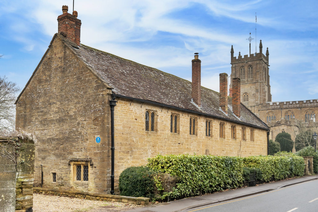 Exterior of a Tudor Court House in Somerset, with sandstone brick and a church tower in the background