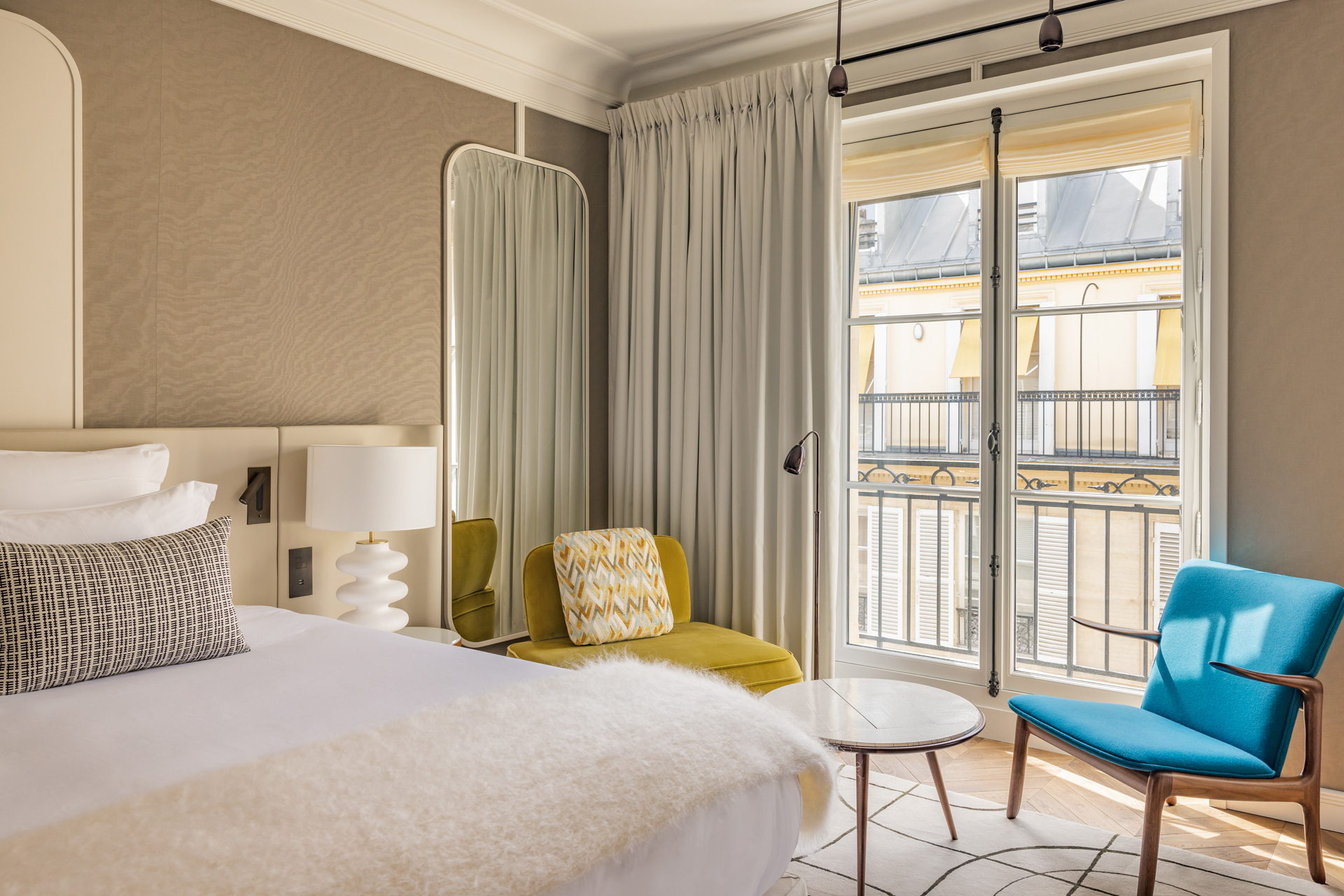 Bedroom at Pavillon Faubourg Saint-Germain in Paris, with white bedding, a blue velvet chair, and a view of typical Parisian apartments outside.