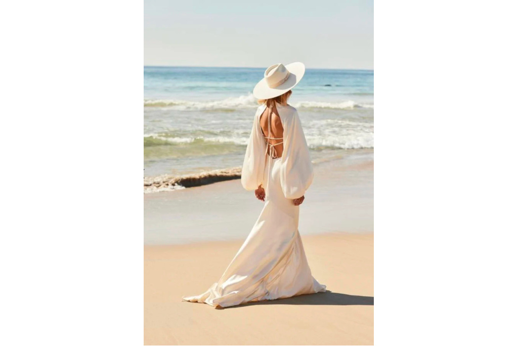 Woman on beach wearing long white dress and hat