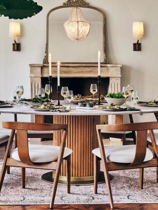 Soho Home ornate gold framed mirror resting on a mantlepiece with a table and chairs in the foreground.