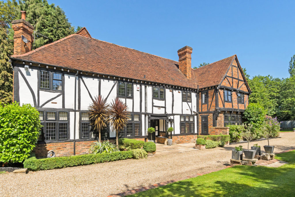 Exterior of a tudor cottage with black exposed beams and greenery surrounding