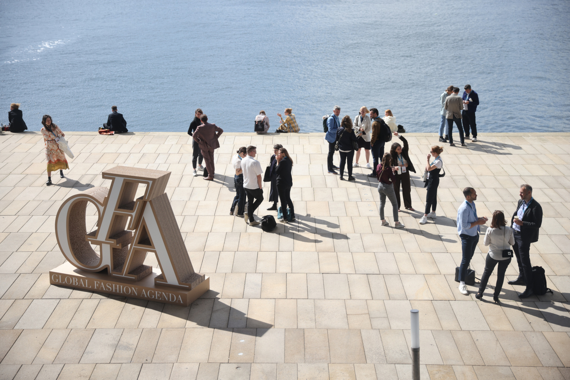 People stood on stone pier overlooking sea by GFA sculpture | Global Fashion Summit 2022