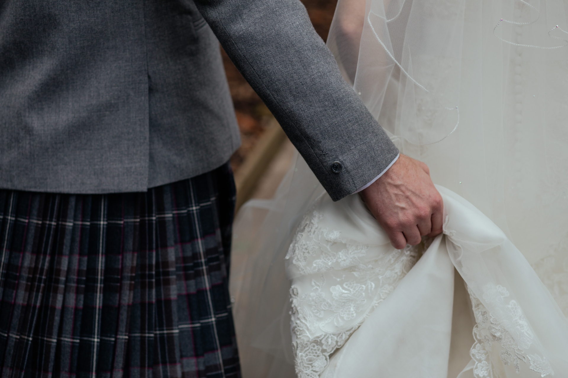 Close up of man in kilt holding train of bride's wedding dress