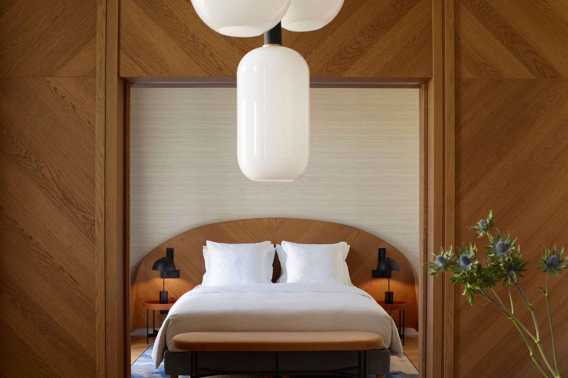 A bedroom in xenodocheio Milos hotel in Athens, with a wooden bed with white sheets framed by a wooden archway.
