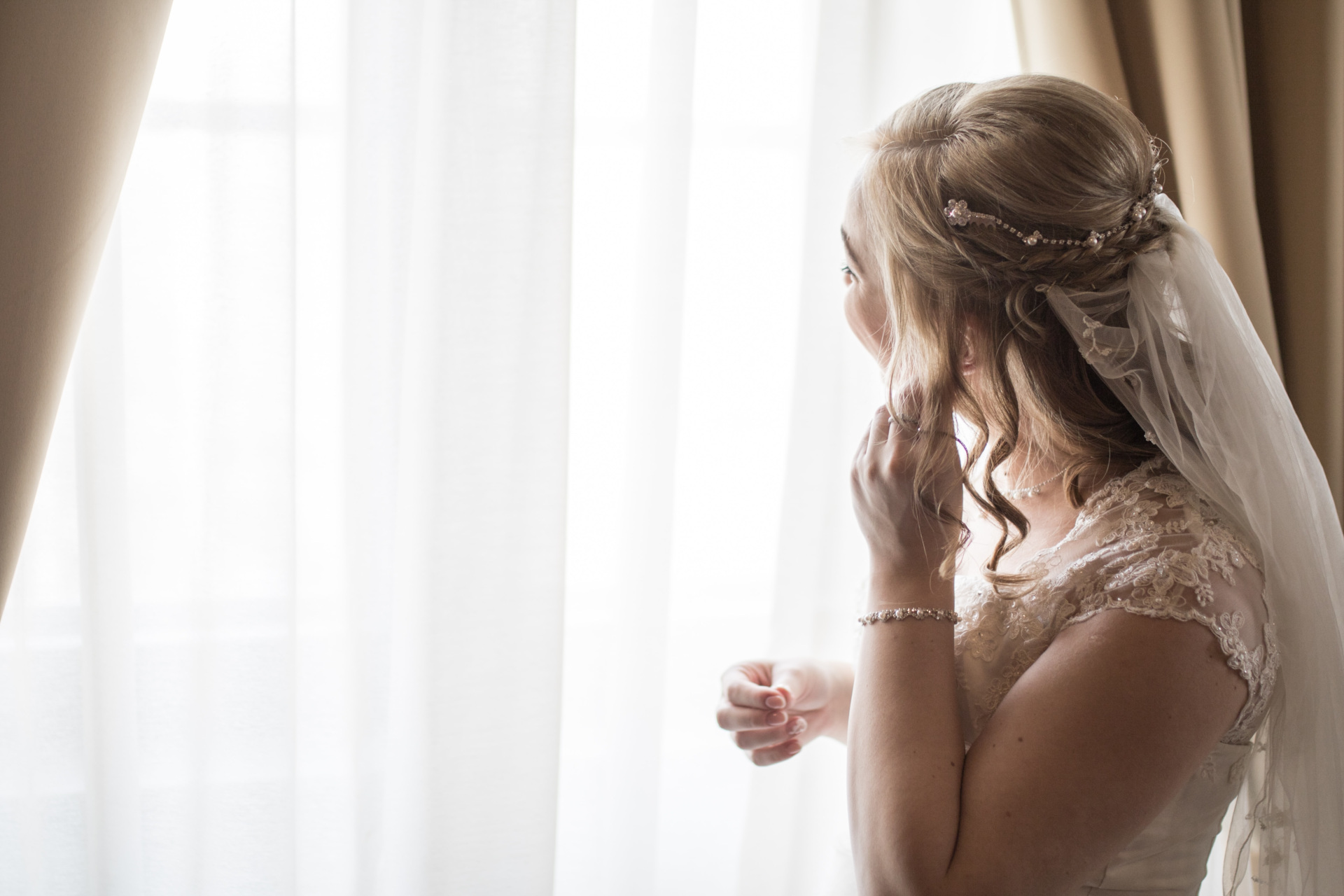 Bride with head turned towards window as she puts on earrings