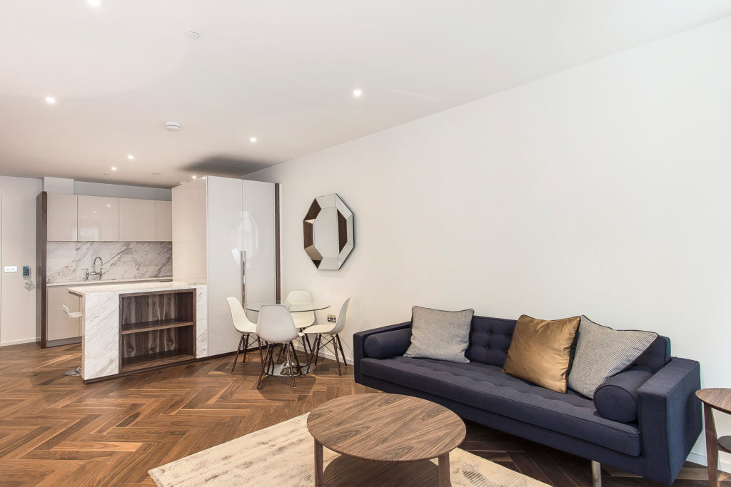 Living room with parquet flooring, black sofa, kitchen with marble worktops, and small circular dining table.