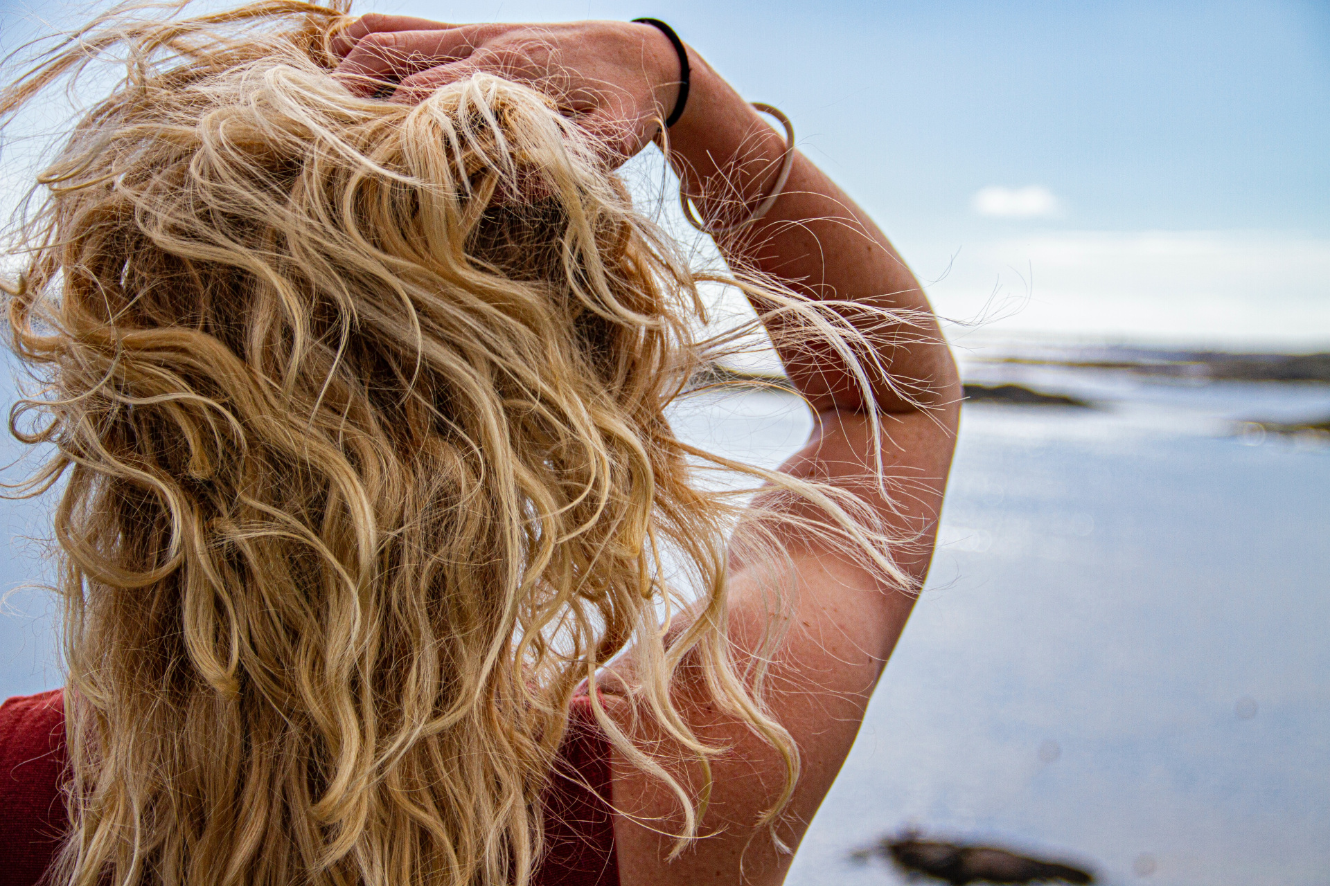 Woman with blonde hair facing away towards ocean