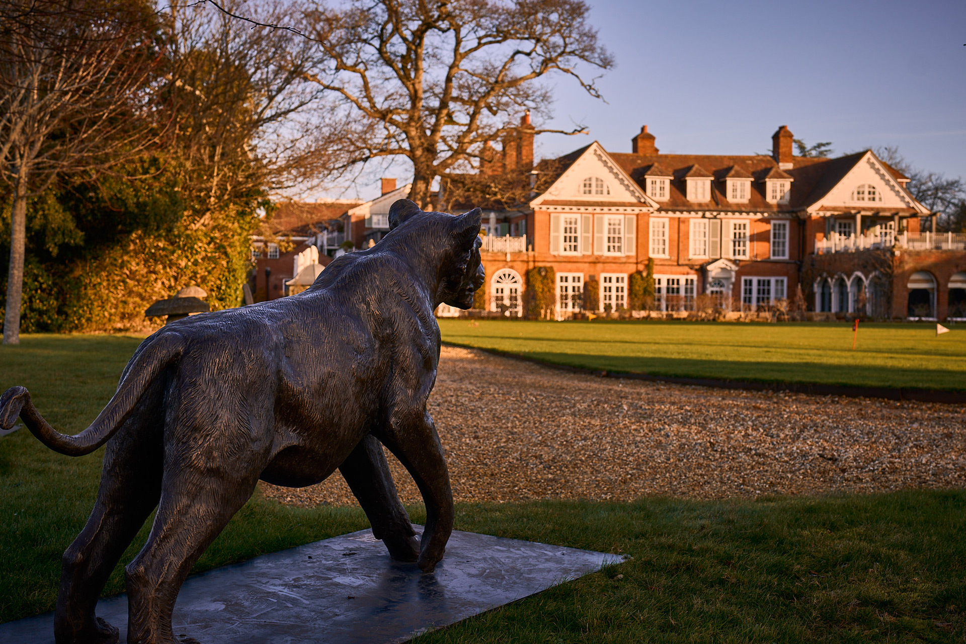 Grand red brick New Forest hotel with prowling lion sculpture in front.