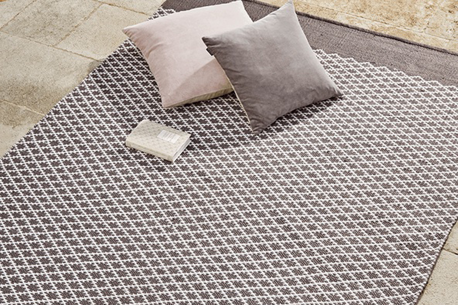 Grey blanket in diamond pattern with matching cushions and a book on top