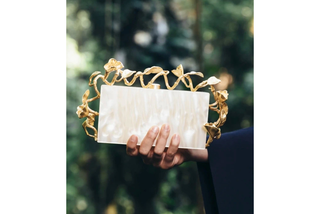 Hand holding ivory clutch with gold detailing