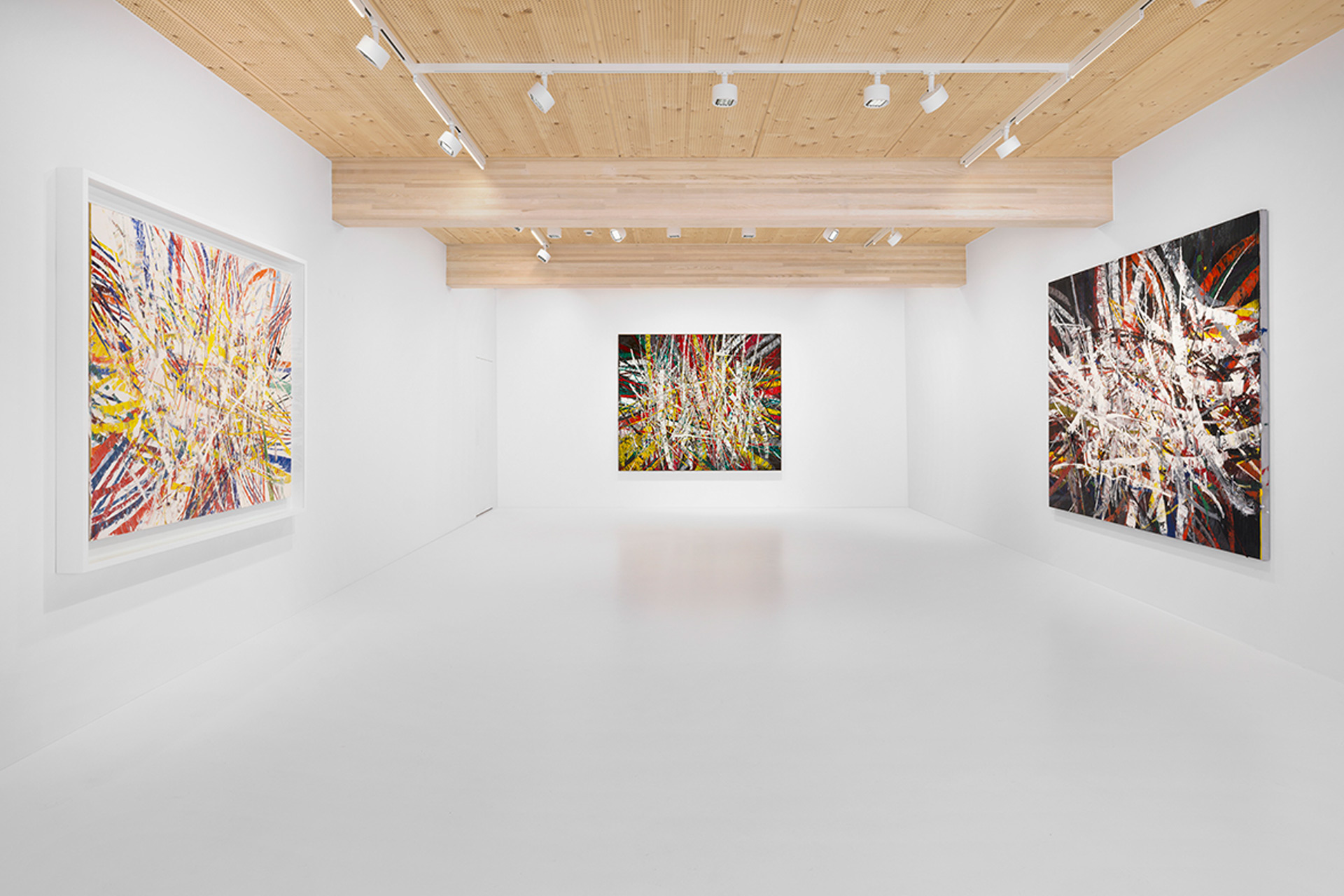 White gallery with light wood-panelled ceiling and abstract prints on the walls.