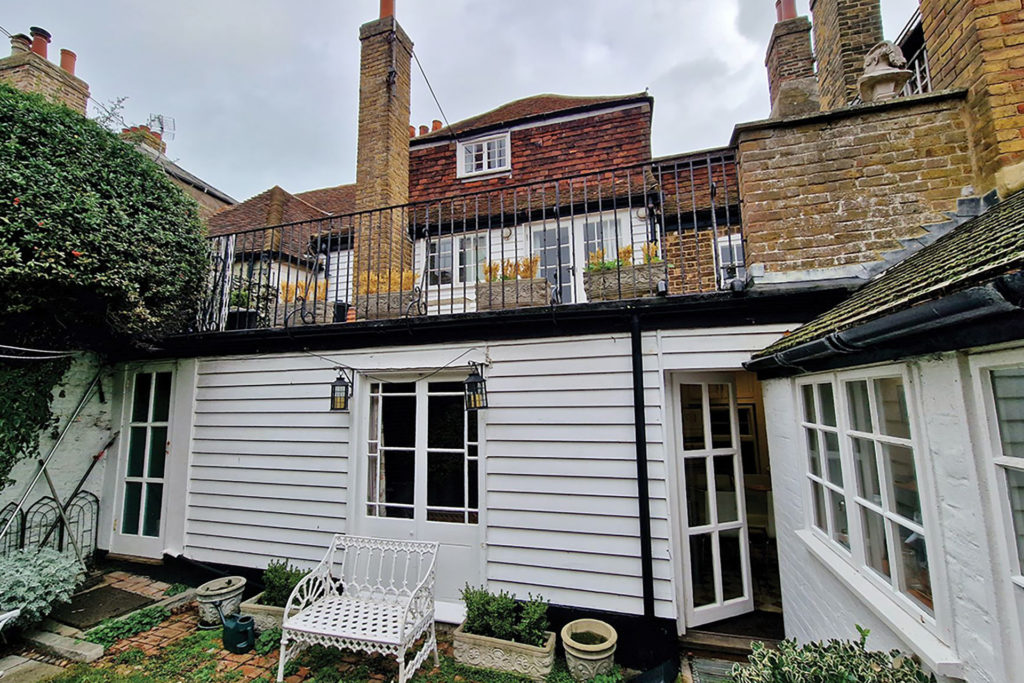 Garden with a terrace above, with fairy lights and white metal furniture