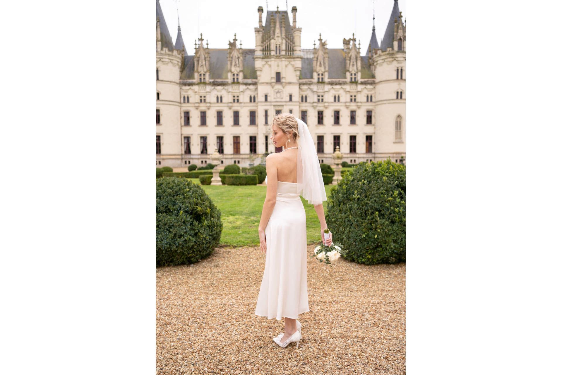 Woman in white dress and veil stood in front of manor