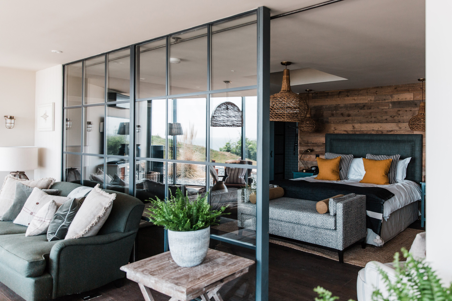 Hotel room with charcoal and burnt orange accents and a crittall-style partition separating a balcony area with grey sofa