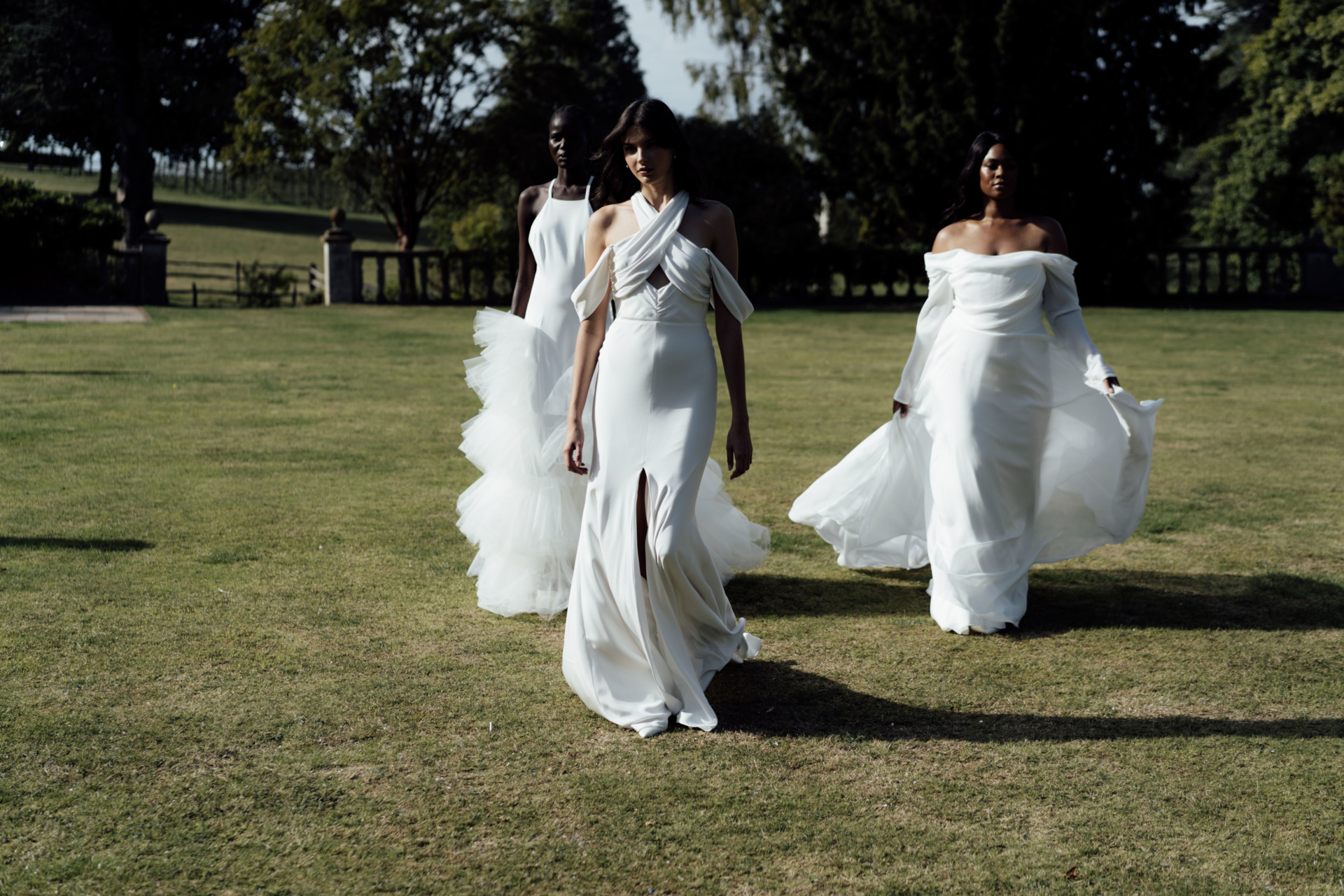 Three women in wedding dresses walking across grass