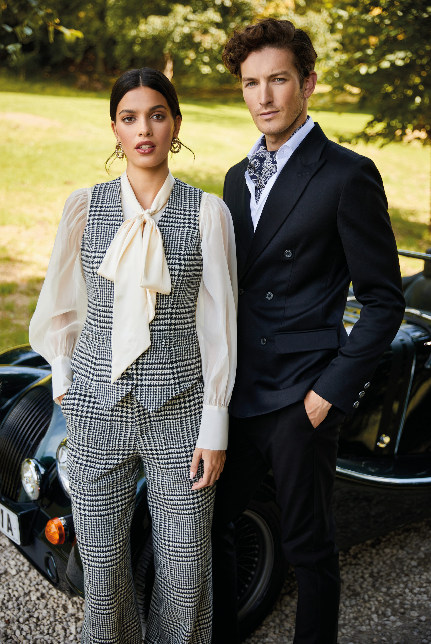 Man and woman in suits stood in front of car and garden