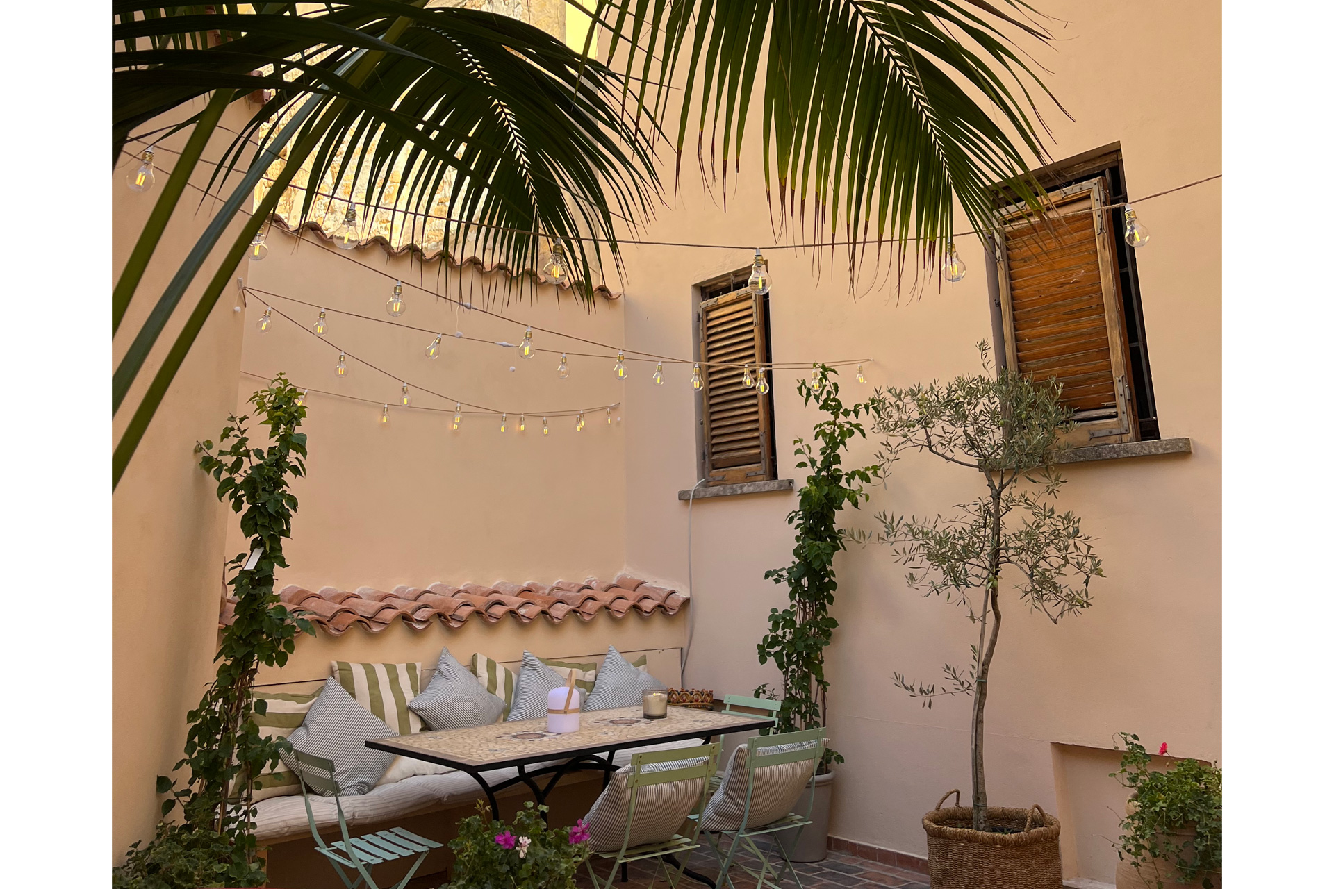 Terrace with pastel yellow walls, striped cushions, and palm trees.