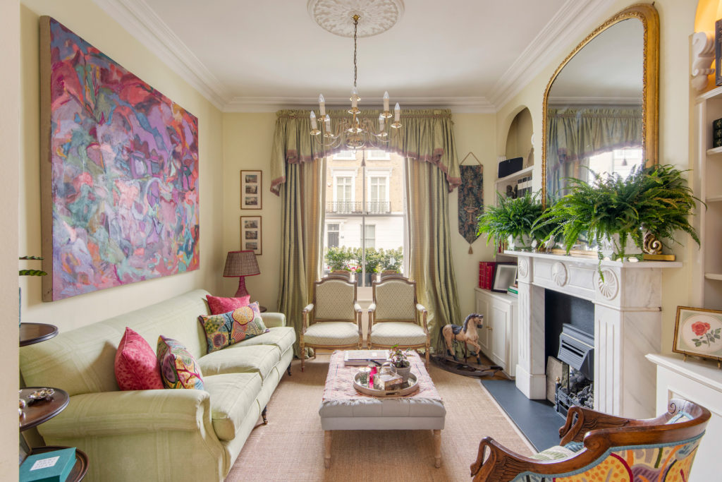 Large living room with a cream sofa and bright pink cushions, an ornate gold mirror and chandelier, and modern artwork with pink and purple paint