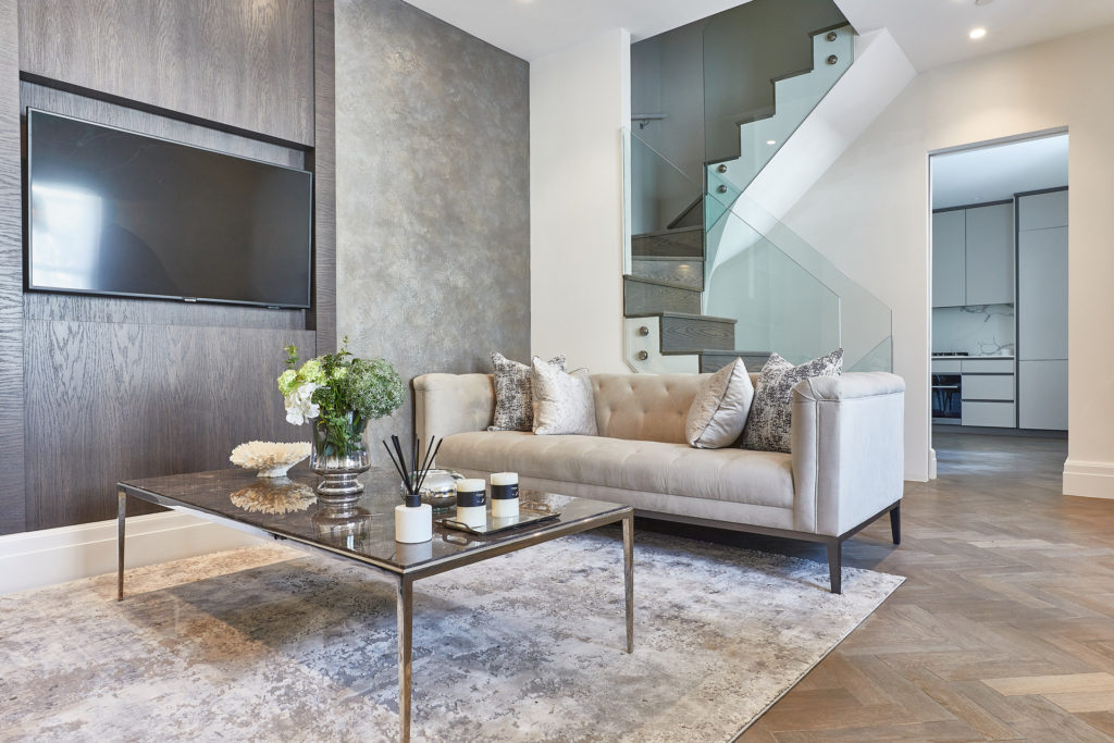 Apartment with wooden flooring, grey crushed velvet rug, cream sofa, and glass-panelled staircase