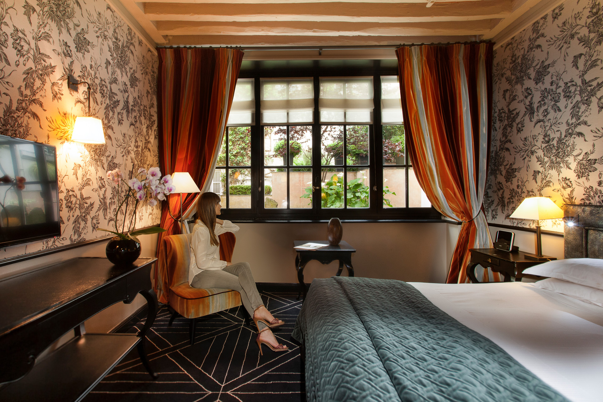 Bedroom at Pavillion de la Reine with floral wallpaper, a green throw on the bed, and orange curtains