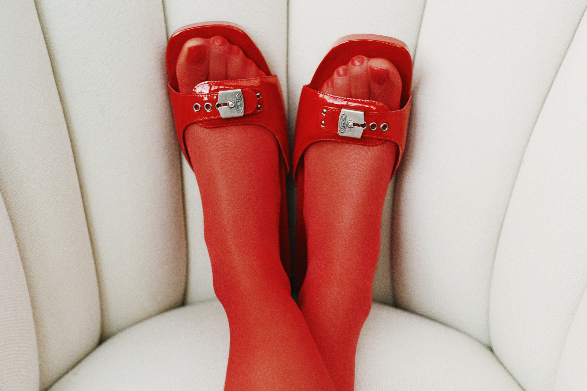 Close up of feet in red tights and shoes on cream armchair