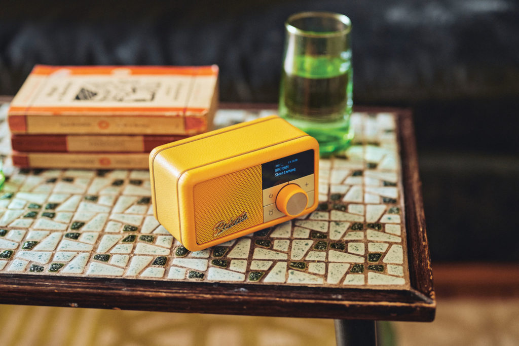 A yellow radio sat on top of a tiled table, there is a stack of books behind it