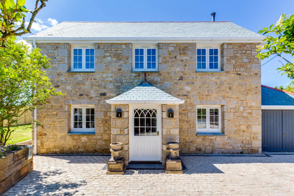Cobblestone cottage with brick porch and driveway in front.