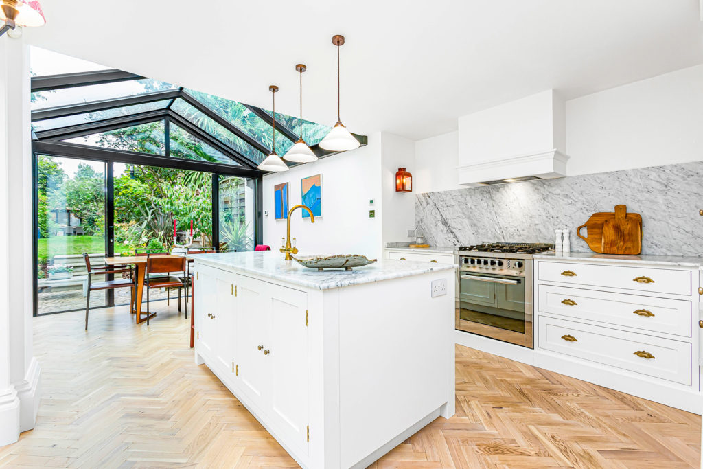 Kitchen with oak flooring and white countertops with a glass-panelled extension