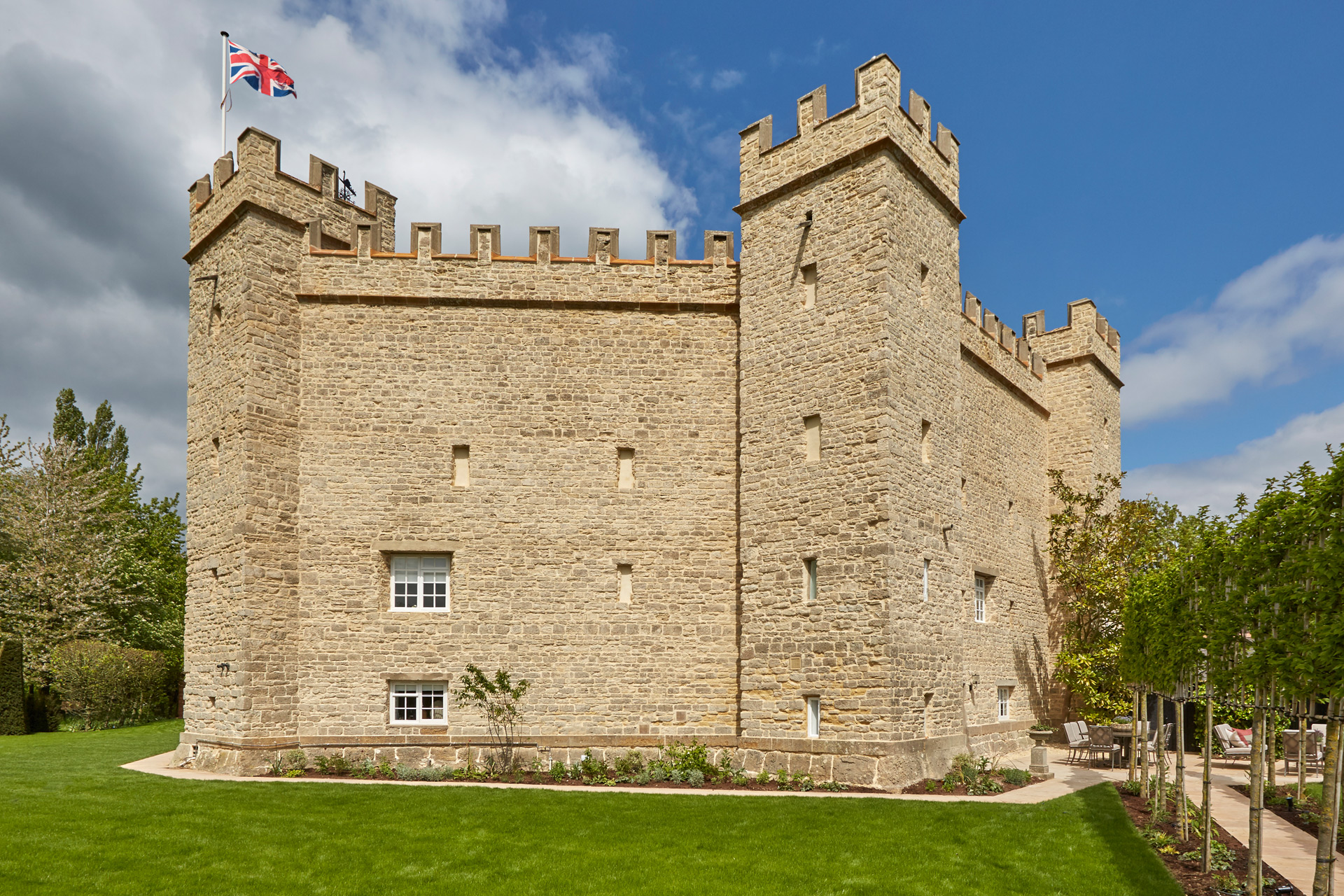 Exterior of castellated house in Stowe with sandstone brick, turrets, and a union jack flag flying from the top