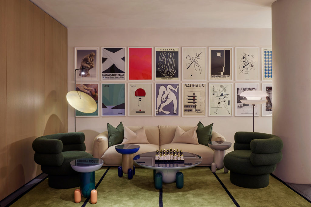 Living area with colourful prints on the walls, cream and green velvet sofas, and a light green marble floor.