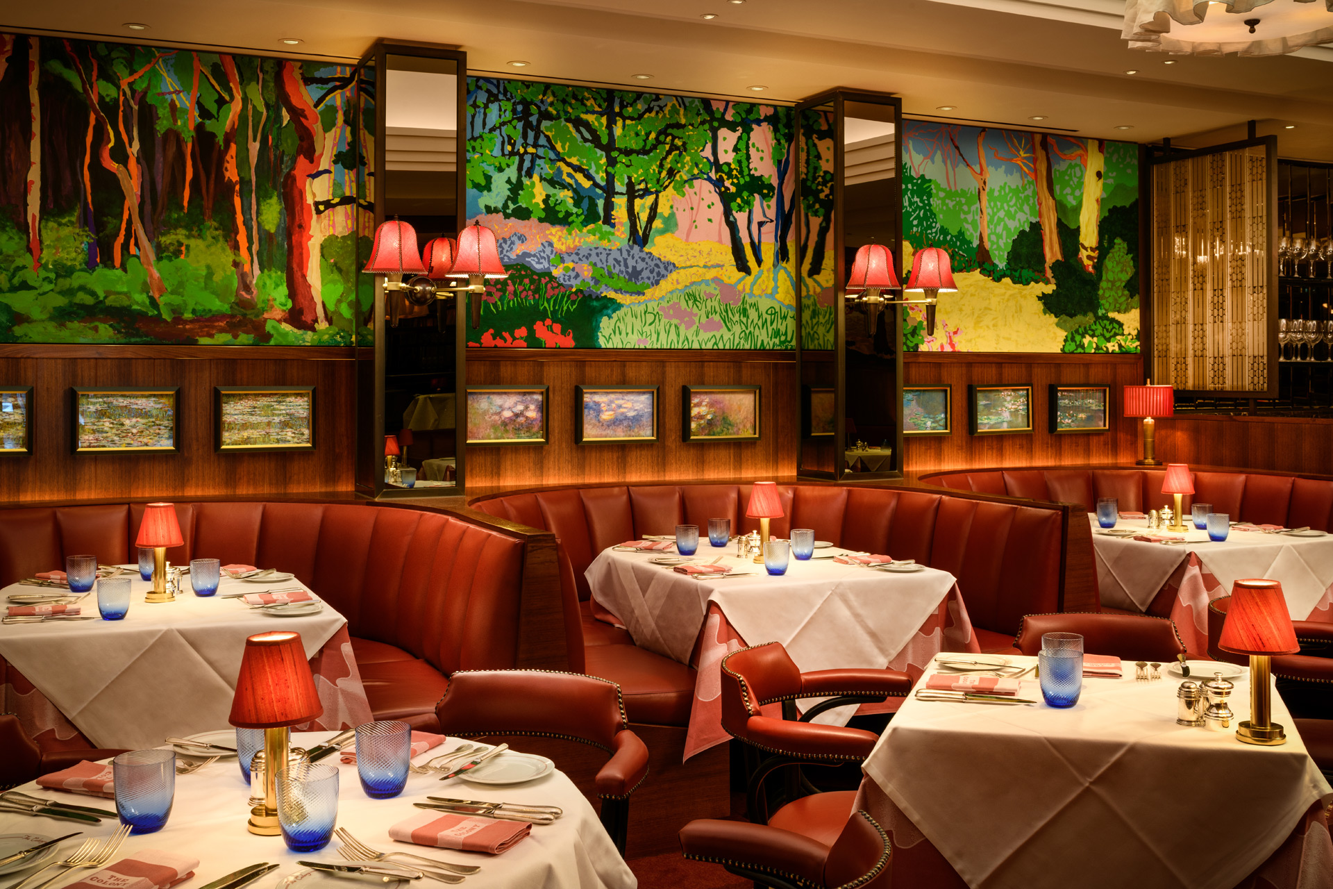 Restaurant with colourful woodland prints, light pink velvet banquette seating and white tablecloths.
