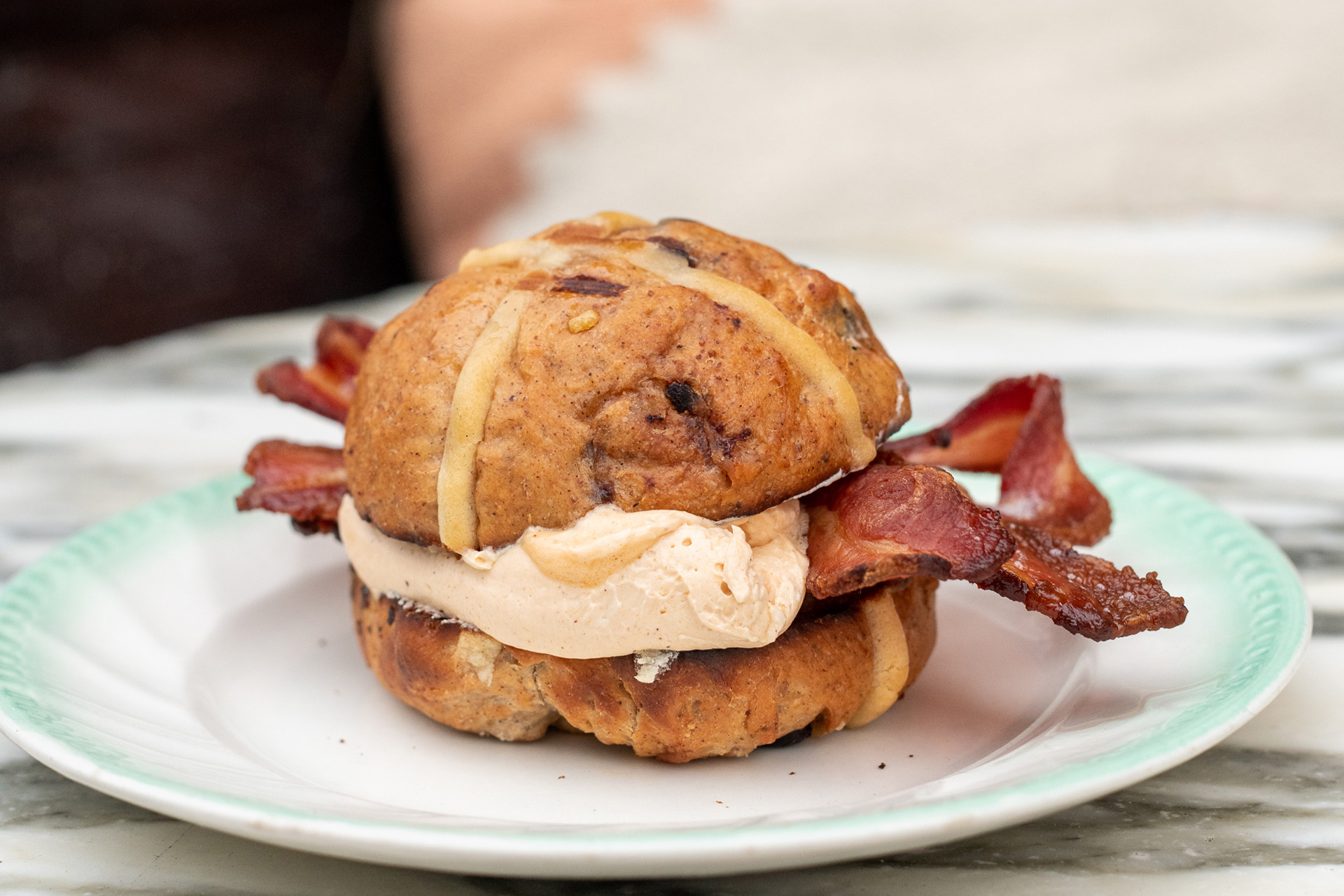 Toasted hot cross bun with a scoop of maple butter and two rashers of bacon.