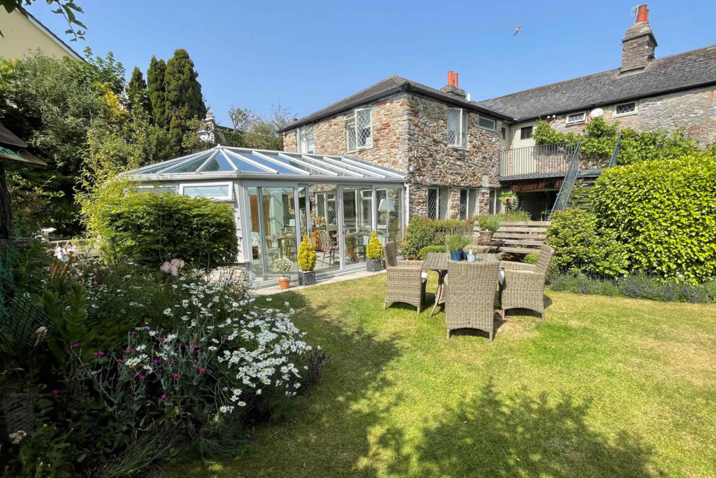 Grassy garden with wicker furniture and view of a grey brick house with conservatory